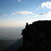 A daring hiker sits on the NE edge of the summit. This part of the summit need not be climbed and is easily avoidable for those afraid of heights.