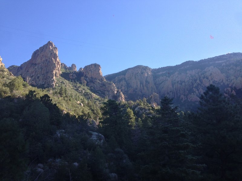 The view of the Sandia ridgeline from the trail, with the tramway cables visible overhead. The upper station of the tramway is visible on the right side of the picture. The crash site is at the base of the large rock formation on the left.