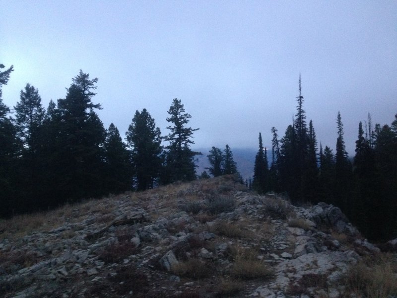 A view of a rocky ridge near the top of the Spring Hollow Trail and the low clouds hanging over the Northern Bear River Range in the distance.