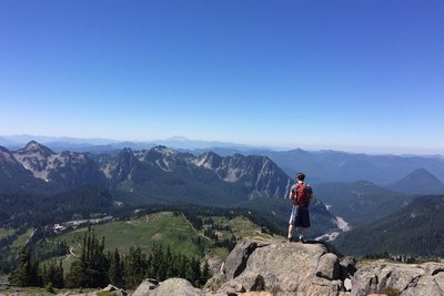 Hiker looking out from Panorama Point while cresting the Skyline Trail. Mount St. Helens looms in the distance.