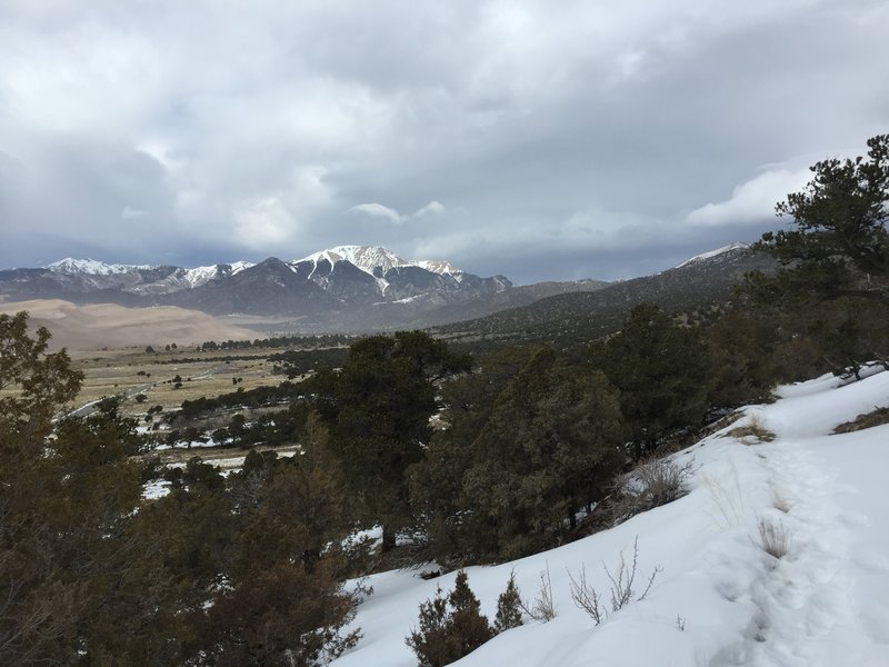 A stormy sky over the mountains and a snowy Wellington Ditch Trail.