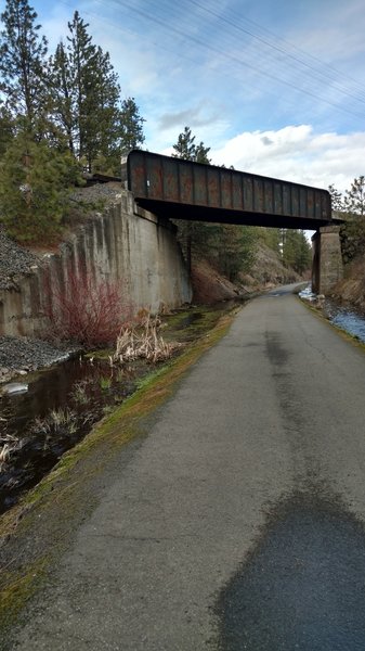 Railroad tracks cross over the trail, stream runs alongside.