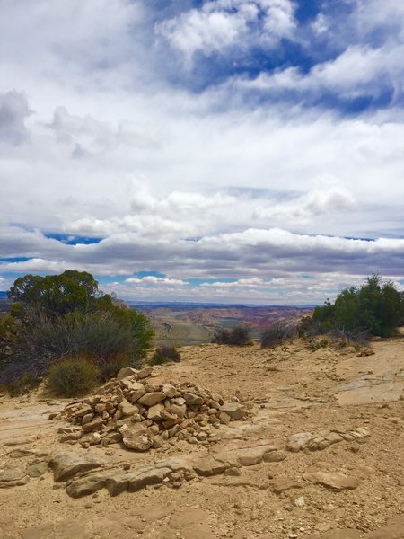 A large rock pile marks the end of the trail at the top of the sandstone cliff viewpoint. The viewpoint spans a few hundred feet in both directions displaying the valley below and mountain ranges in the distance.