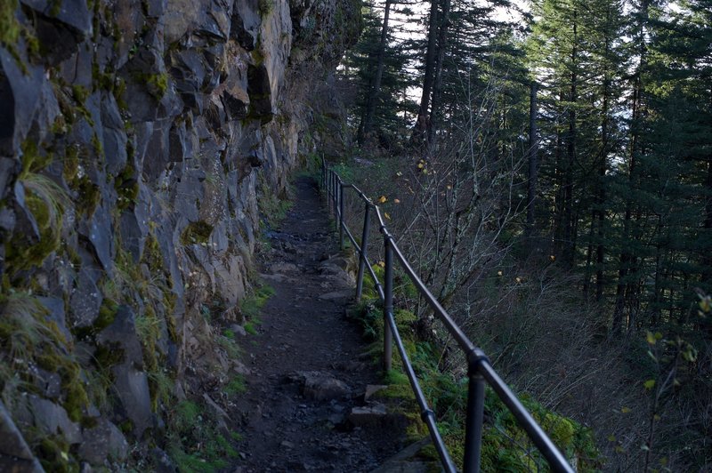 The trail follows the rock face of the cliff as it makes its way toward the falls. This is looking back down the trail.