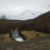 The downstream side of the dam harbors dense hardwood forests and a raging outflow.