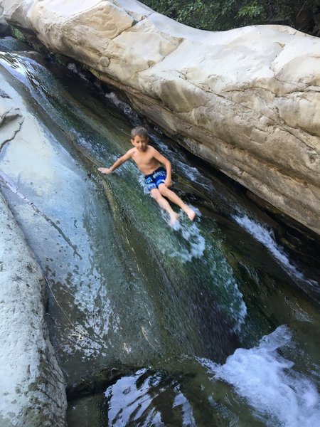 A kid slides on the rocks next to Cross Camp.