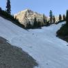 Mt. Timpanogos looms over the the last snowfield crossing before a hiker and his dog reach Timpanogos Basin.