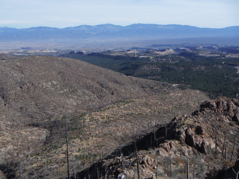 On Rendija Ridge looking east down the ridgeline trail. Santa Fe Baldy in the Sangre de Cristo Mountains north of Santa Fe is in the center of the background. Los Alamos townsite is in the right foreground.