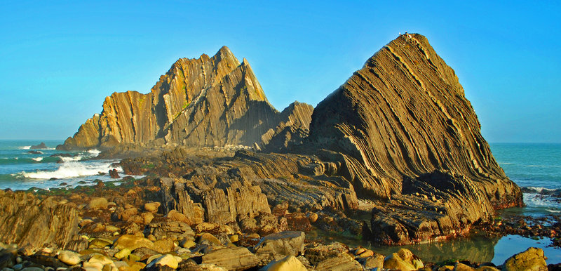 San Pedro Rock in the background, which can be hiked to at extreme low tide via a chain of 3 small islands. The Pilarcitos Fault has pushed the thick sedimentary layers nearly vertical and sheared them off on the north side