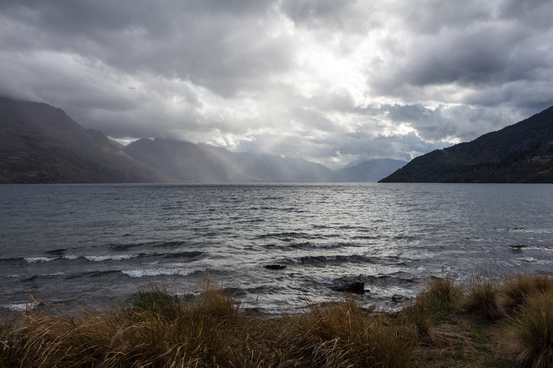 The sun breaking through the clouds on the rainy day looking across Lake Wakatipu