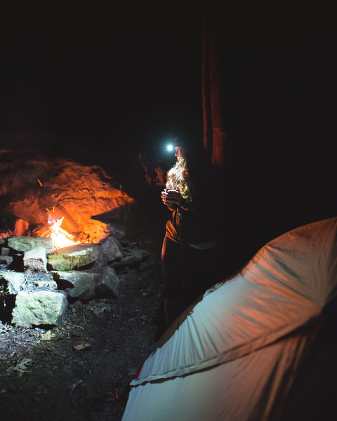 Travel companion drinking some late night tea next to a fire, in one of the backcountry camping sites at Cloudland State Park.