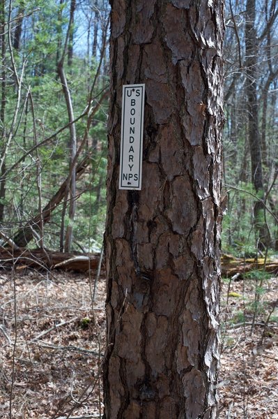 The park boundary is marked by a simple sign on a tree next to the trail. The trail continues on for a short distance to the road.