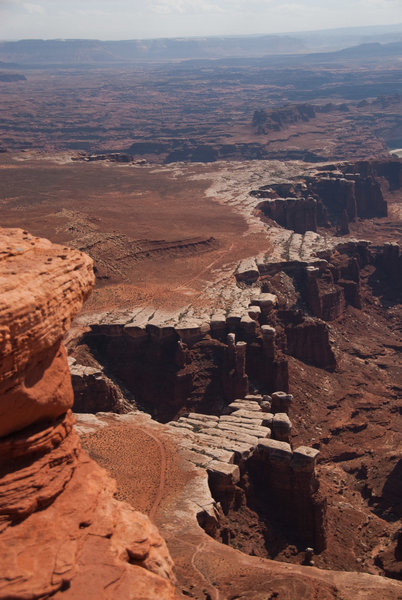 Two bicyclists pausing on White Rim Road give scale to Monument Basin (lowermost section of the rim 1/3 from the right edge of the photo).