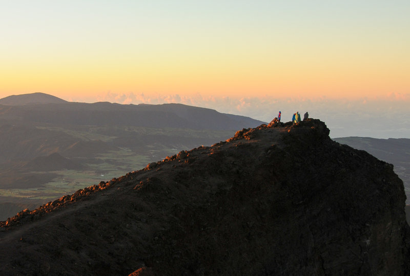 Some hikers enjoy sunrise on Piton des Neiges' sub-peak with Piton de la Fournaise in the far distance.