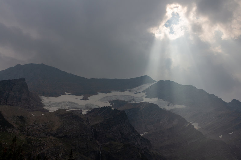 The sun breaks through the clouds and smoke above Gunsight Mountain