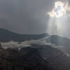 The sun breaks through the clouds and smoke above Gunsight Mountain