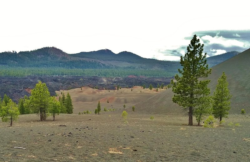 Light colored Painted Dunes (center) at the base of Cinder Cone (north side) on the right, with the black boulders of Fantastic Lave Beds behind them. In the distance are Ash Butte (left), Red Cinder Cone/Red Cinder (center), and Mt Hoffman (right).