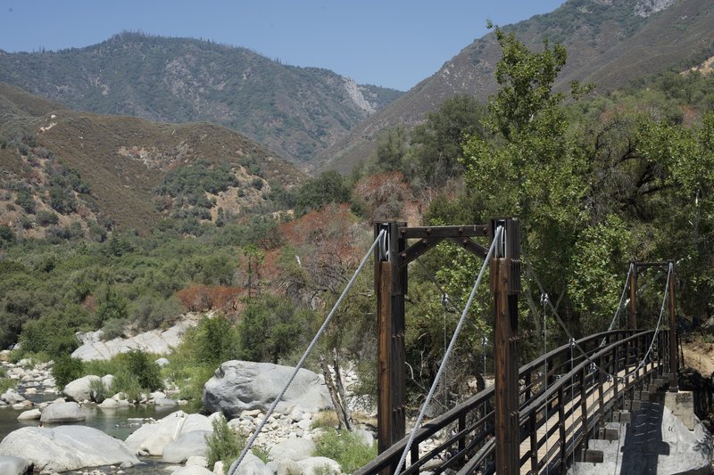 The swinging bridge crossed the river.  The river is a popular spot in the summer as people try to cool off.