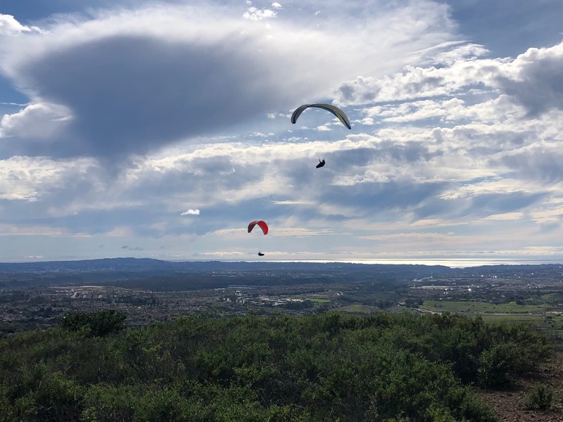 Two paragliders on the western edge of Black Mountain with Torrey Highland in the distance and the Pacific Ocean 10 miles away. Downtown La Jolla is just left of the lower paraglider.