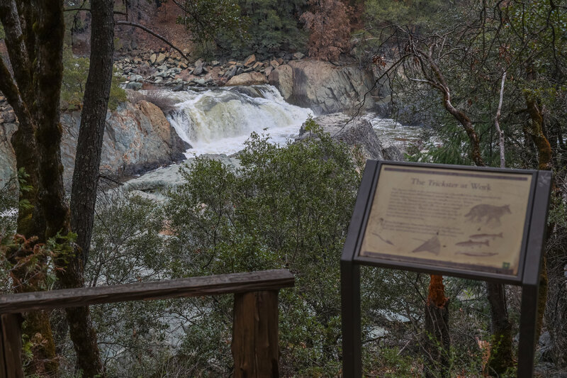 A wooden bench and interpretive sign appear at the first view of Indian Creek Falls.