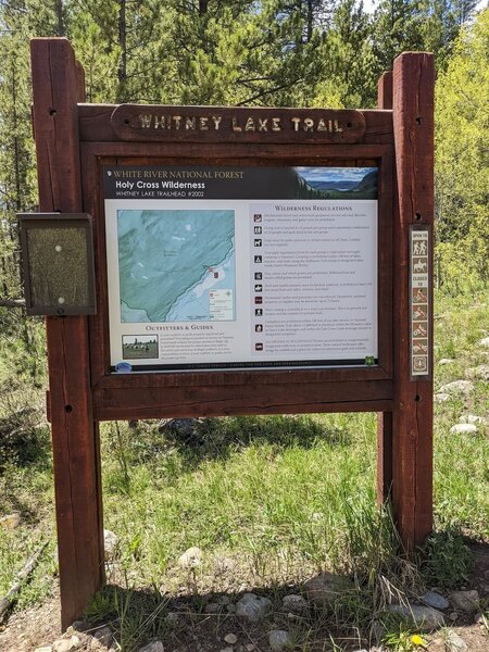 Whitney lake trailhead sign, it's partially obscured by trees from the road.