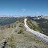 The trail runs on a high ridge of the Great Divide here, with a slow melting cornice to the right, cracked, could fall down the cliff. In the distance are Font Mountain (right center) and Mount Matkin (right). Seen looking west-northwest.