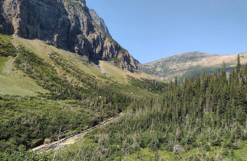 Siyeh Creek (lower left) runs in the valley below.  Massive cliffs (left) of the east face of Piegan Mountain, 9,219 ft., rise above the creek.