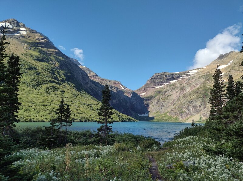 Gunsight Lake and wildflowers.  Gunsight Pass over the Continental Divide is in the distance (center), with Gunsight Mountain to its right/northwest, and Mount Jackson to its left/southeast. Seen looking southwest at Gunsight Lake trail camp.