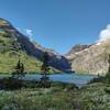 Gunsight Lake and wildflowers.  Gunsight Pass over the Continental Divide is in the distance (center), with Gunsight Mountain to its right/northwest, and Mount Jackson to its left/southeast. Seen looking southwest at Gunsight Lake trail camp.