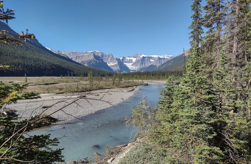 A side channel of the Alexandra River below in the river's broad, flat valley. Mountains and the Alexandra Glaciers to the southwest, are in the distance. Zoom in for a close up look of the Great Divide.