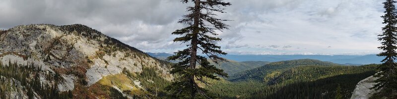 Impressive unnamed mountain to the north (on the left). Forested foothills and the Kootenai River Valley below to the east (on the right), with the Purcell Mountains hidden in the clouds on the horizon as their backdrop.