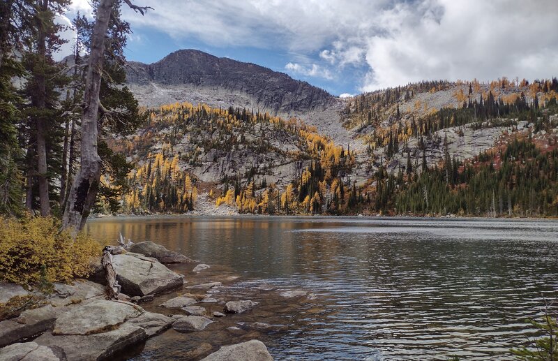 The upper/third Roman Nose Lake in its rugged cirque. At its far end, sun lights up the dazzling yellow larch trees of October. Roman Nose Peak, 7,260 ft., stands above the cliffs.