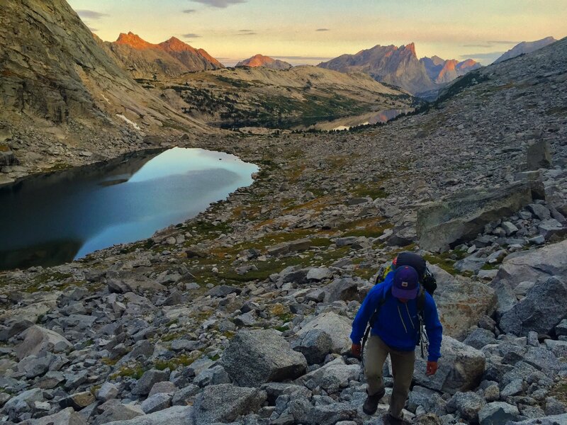 Walking up to the base of Lost Temple Spire. Sunrise lighting up the peaks of the Cirque of Towers in the distance.