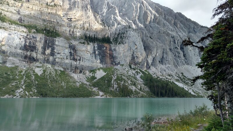 The trail runs along the south shoreline of turquoise Upper Elk Lake. Mt Fox, 9.754 ft., with its cliffs, dominates the north side of the east end of the lake.