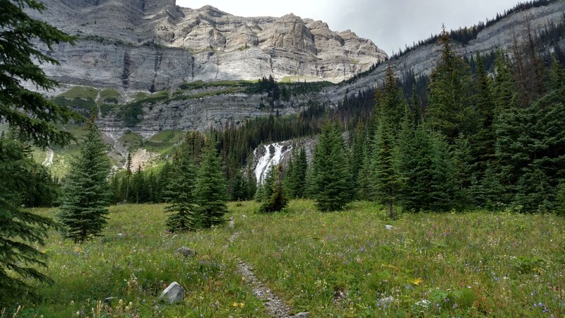 Crossing a grassy meadow when approaching Petain Falls in its amphitheater of waterfalls.